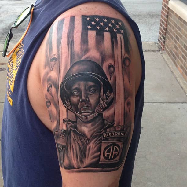 A powerful American flag tattoo featuring a soldier from the Airborne division, with detailed shading and realism. The design includes the U.S. flag in the background, with paratroopers descending, symbolizing bravery, patriotism, and dedication to service. The tattoo is prominently placed on the upper arm, showcasing the wearer's pride in their military background.