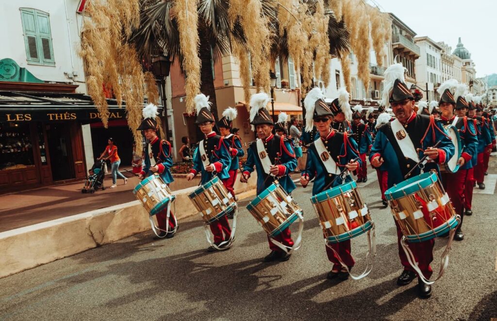 A vibrant military band performing in a street parade, dressed in ornate blue and red uniforms with feathered hats, as part of a European Military Tattoo Show. This image captures the lively atmosphere and rich traditions that are central to Military Tattoo Shows across Europe.