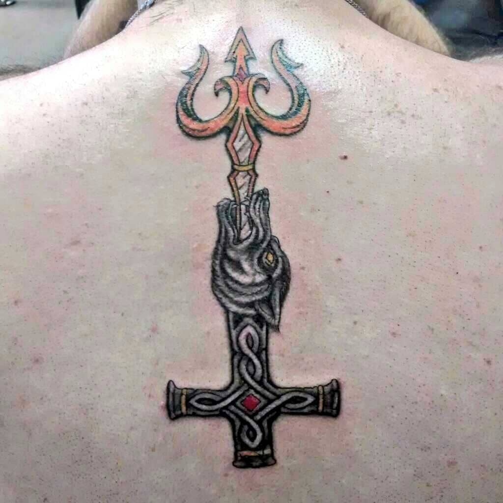 A detailed trident tattoo design on the upper back, featuring a three-pronged trident with an ornate handle. The trident is held by a stylized hand, and the design incorporates elements of Celtic patterns with vibrant orange and red accents on the trident's prongs. The tattoo symbolizes power, strength, and protection, with intricate detailing enhancing the overall impact.