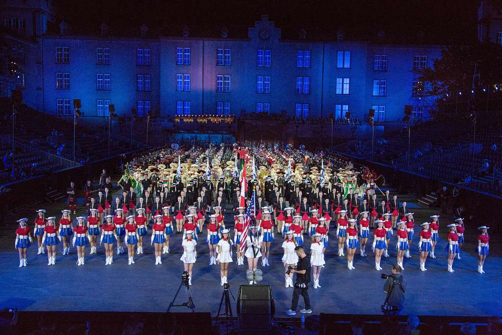 A grand performance at the Basel Tattoo, featuring a diverse group of military bands and performers in colorful uniforms, all gathered in formation in front of a beautifully lit building. This image highlights the international collaboration and pageantry that make the Basel Tattoo so special.