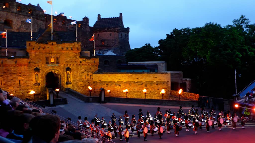 A military band performing in front of Edinburgh Castle during the Royal Edinburgh Military Tattoo, an event that exemplifies the tradition of military displays known as tattoos, with origins rooted in the 17th-century practice of signaling soldiers to return to their barracks. This image captures the essence of why a military display is called a tattoo.