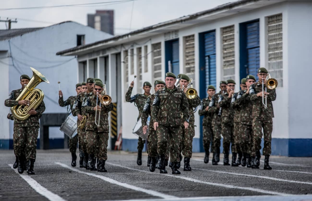 A famous military band dressed in camouflage uniforms and green berets, marching in formation while playing brass and percussion instruments during a military tattoo event.