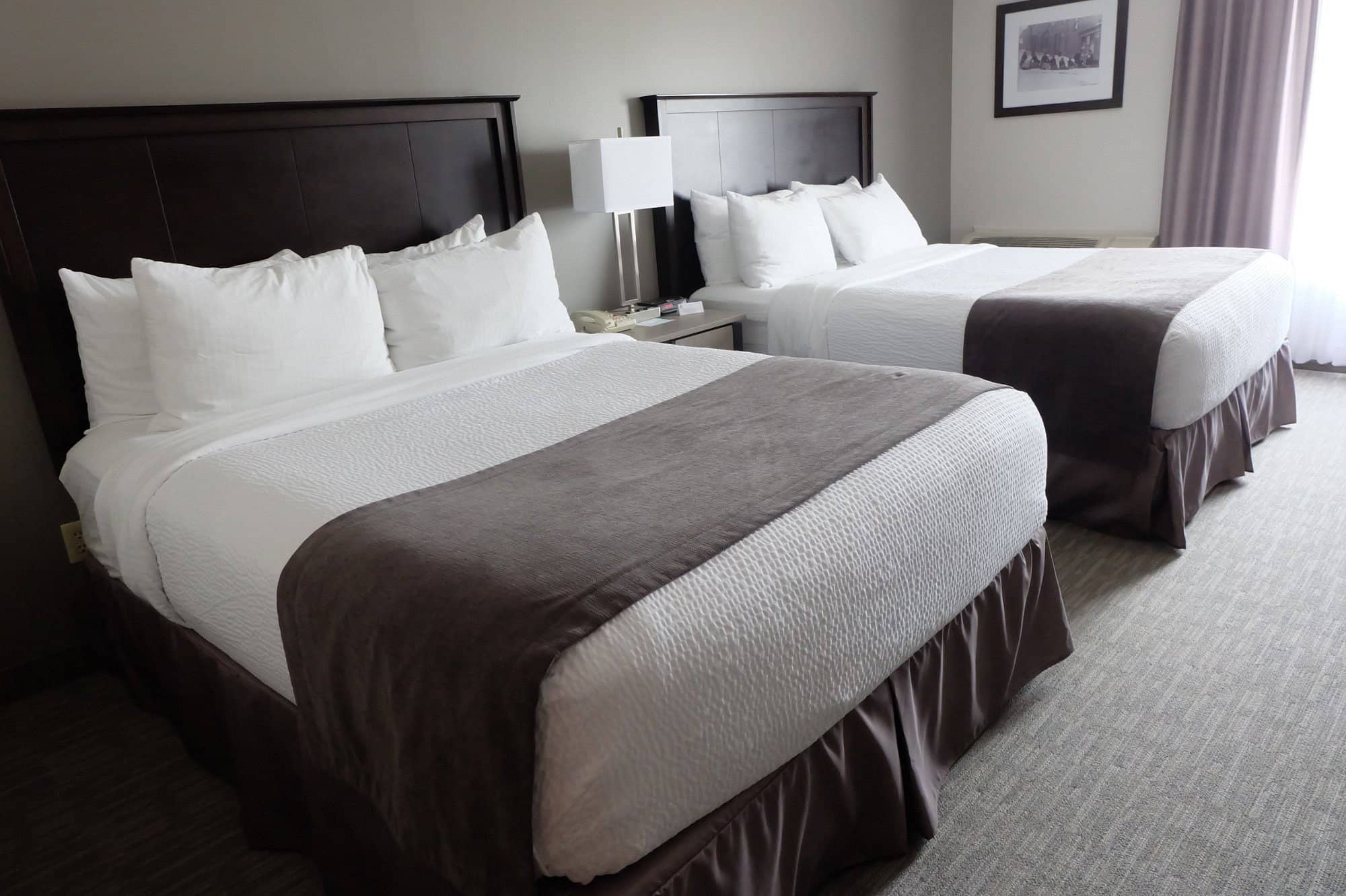 Modern room at Chateau Bedford Trademark Collection by Wyndham featuring two queen beds with white linens and grey accents Room has neutral tones and simple decor