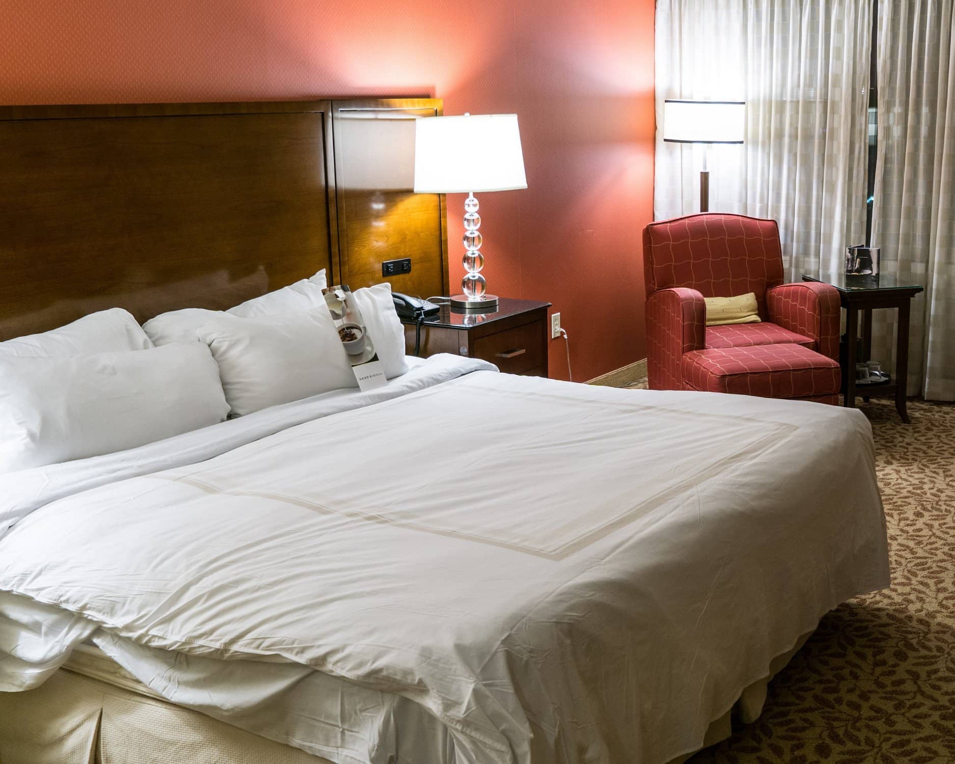 Cozy and warm room at Halifax Marriott Harbourfront Hotel featuring a king-size bed with plush white linens a bedside table with a modern lamp and a comfortable red armchair in the corner ideal for relaxation