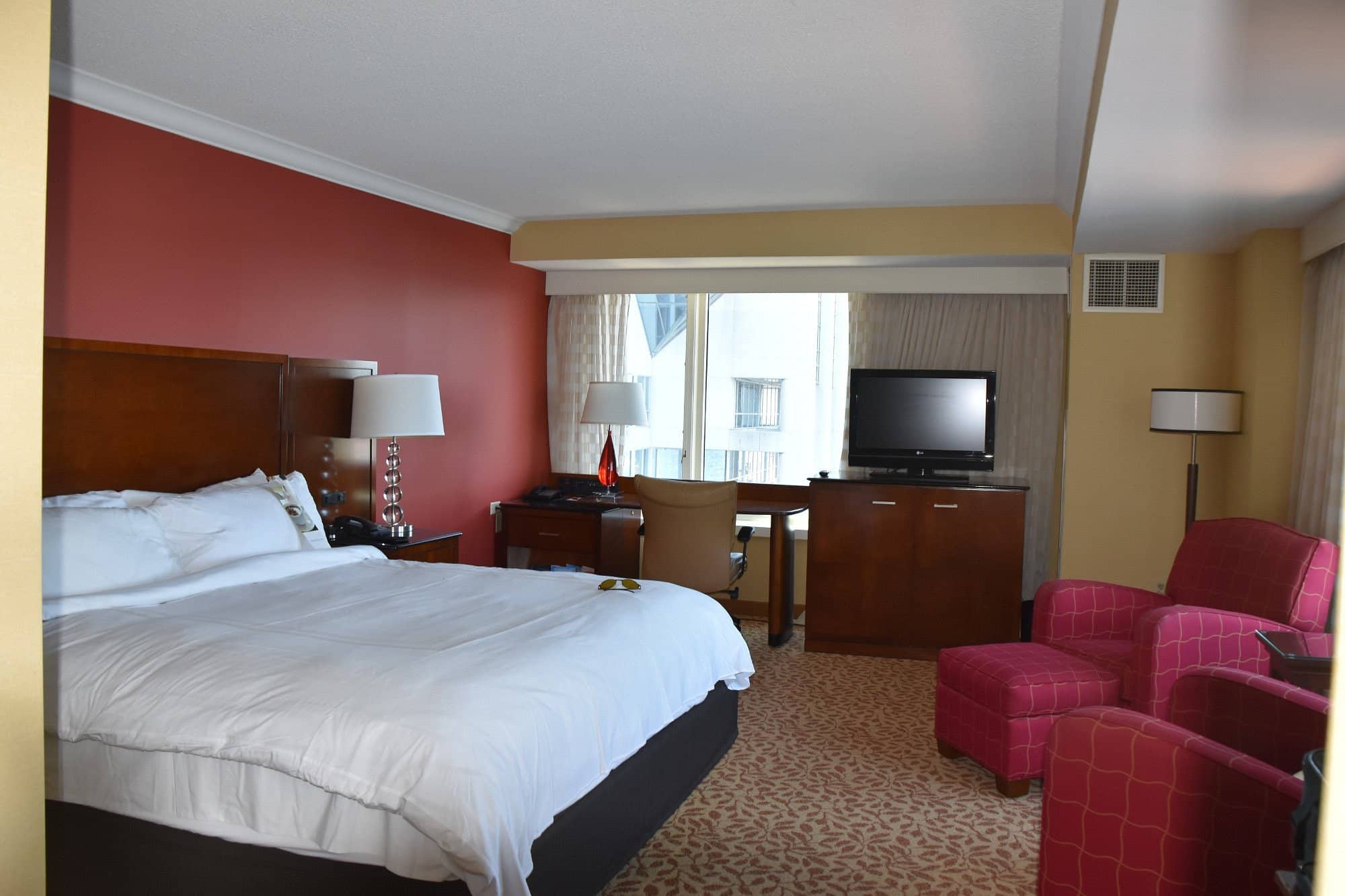 Bright and cozy room at Halifax Marriott Harbourfront Hotel featuring a king-sized bed warm red accents a desk area with a comfortable chair TV and inviting armchairs for relaxation