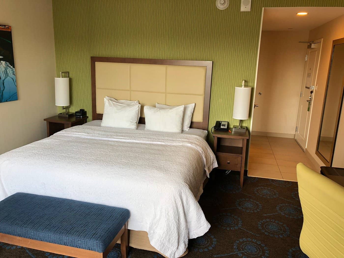 Modern guest room at Hampton Inn by Hilton HalifaxDowntown featuring a king-size bed nightstands a bench and vibrant green decor