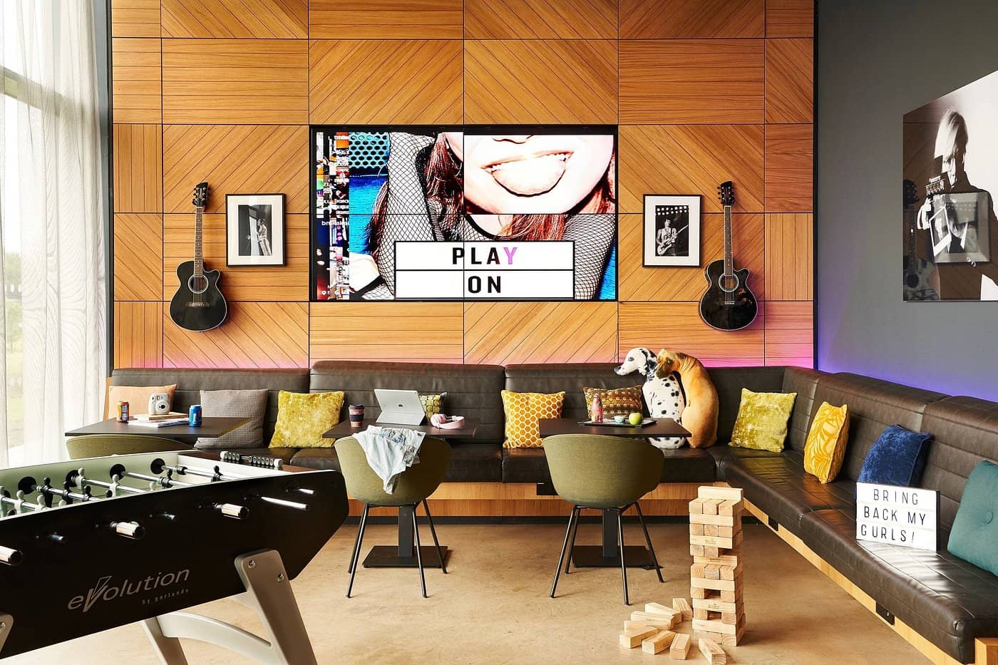 A vibrant and modern lounge area at Moxy Edinburgh Airport featuring cozy seating playful decor with guitars and interactive elements like a foosball table providing a lively and inviting space for guests