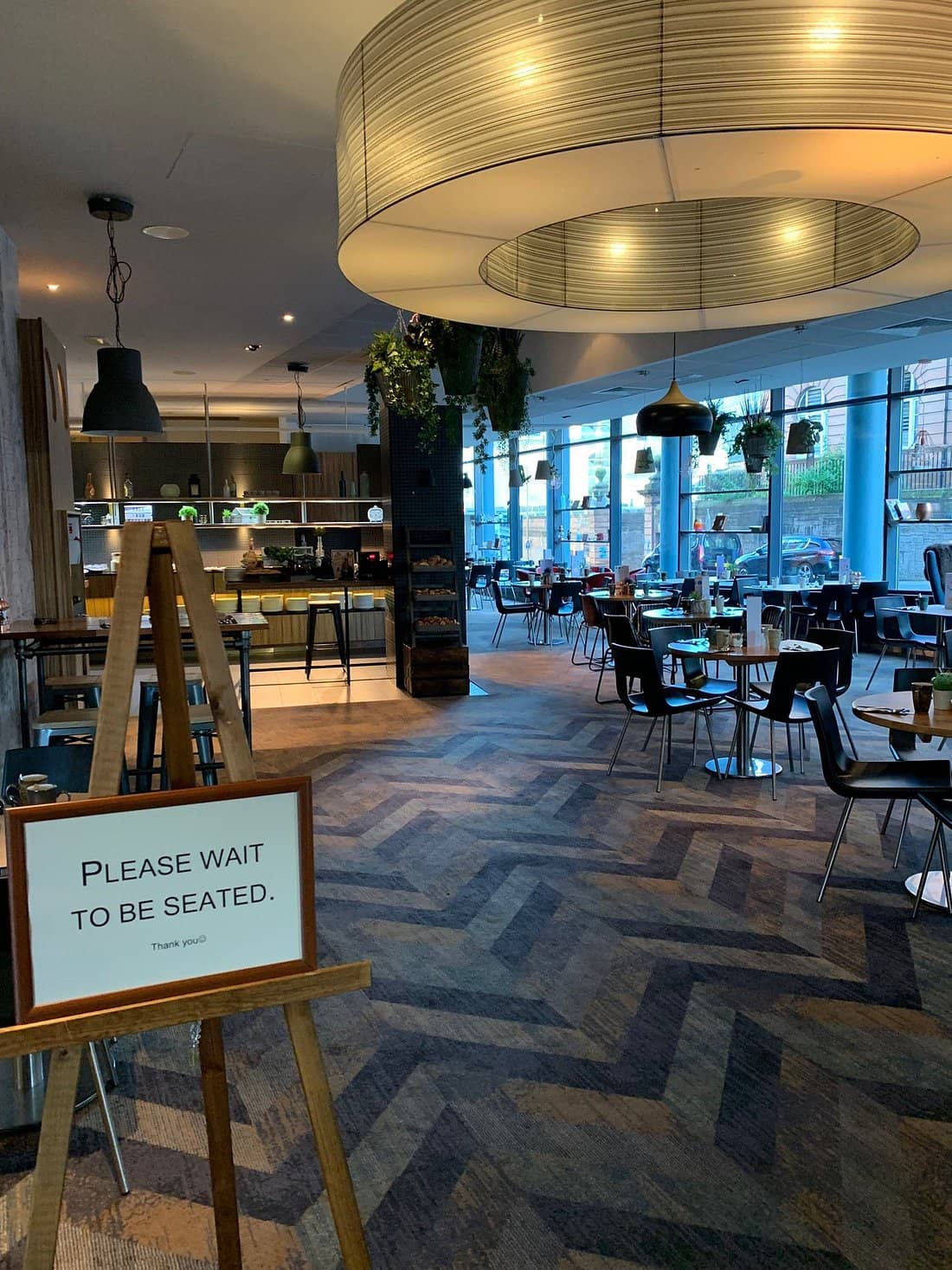  Dining area at Novotel Edinburgh Centre featuring modern decor with large windows stylish lighting and a Please Wait to Be Seated sign providing a welcoming ambiance for guests