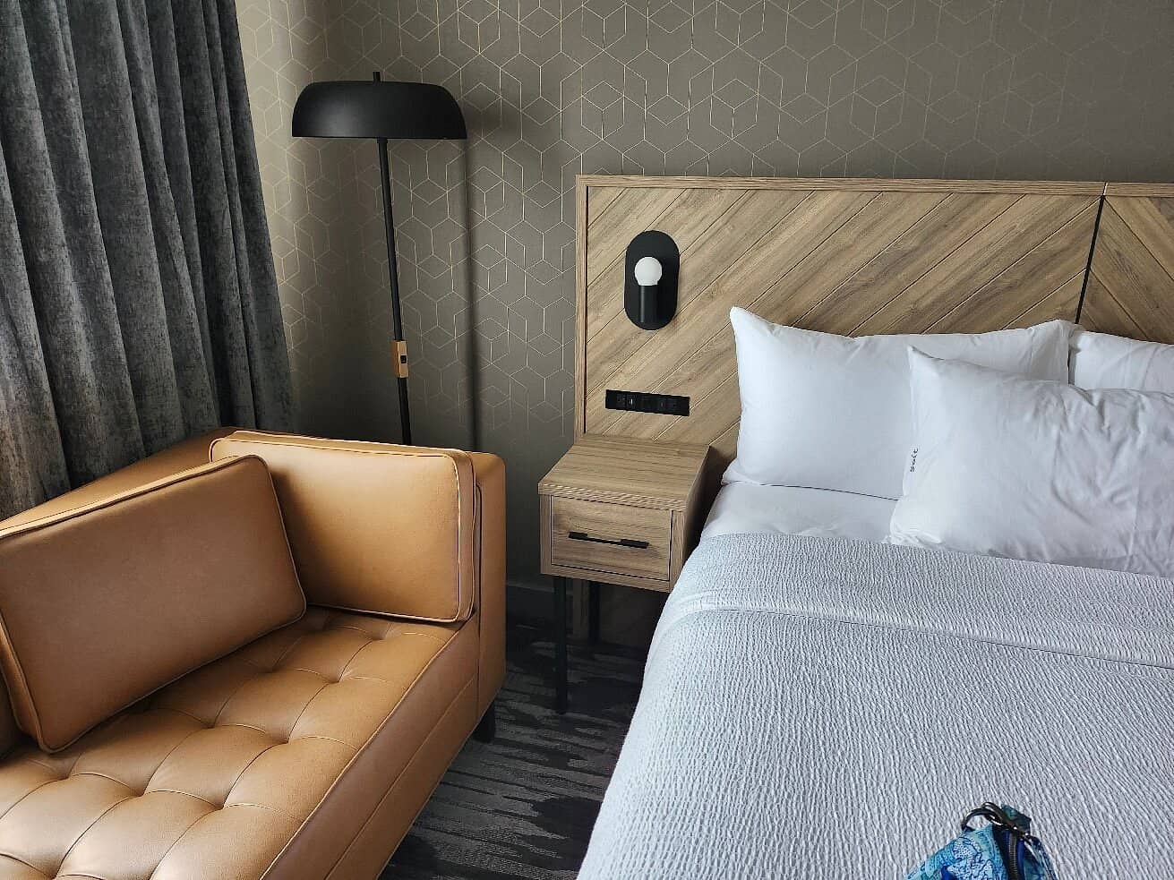 Modern room with a cozy bed wooden headboard and a tan leather sofa at Sandman Signature Dartmouth Hotel