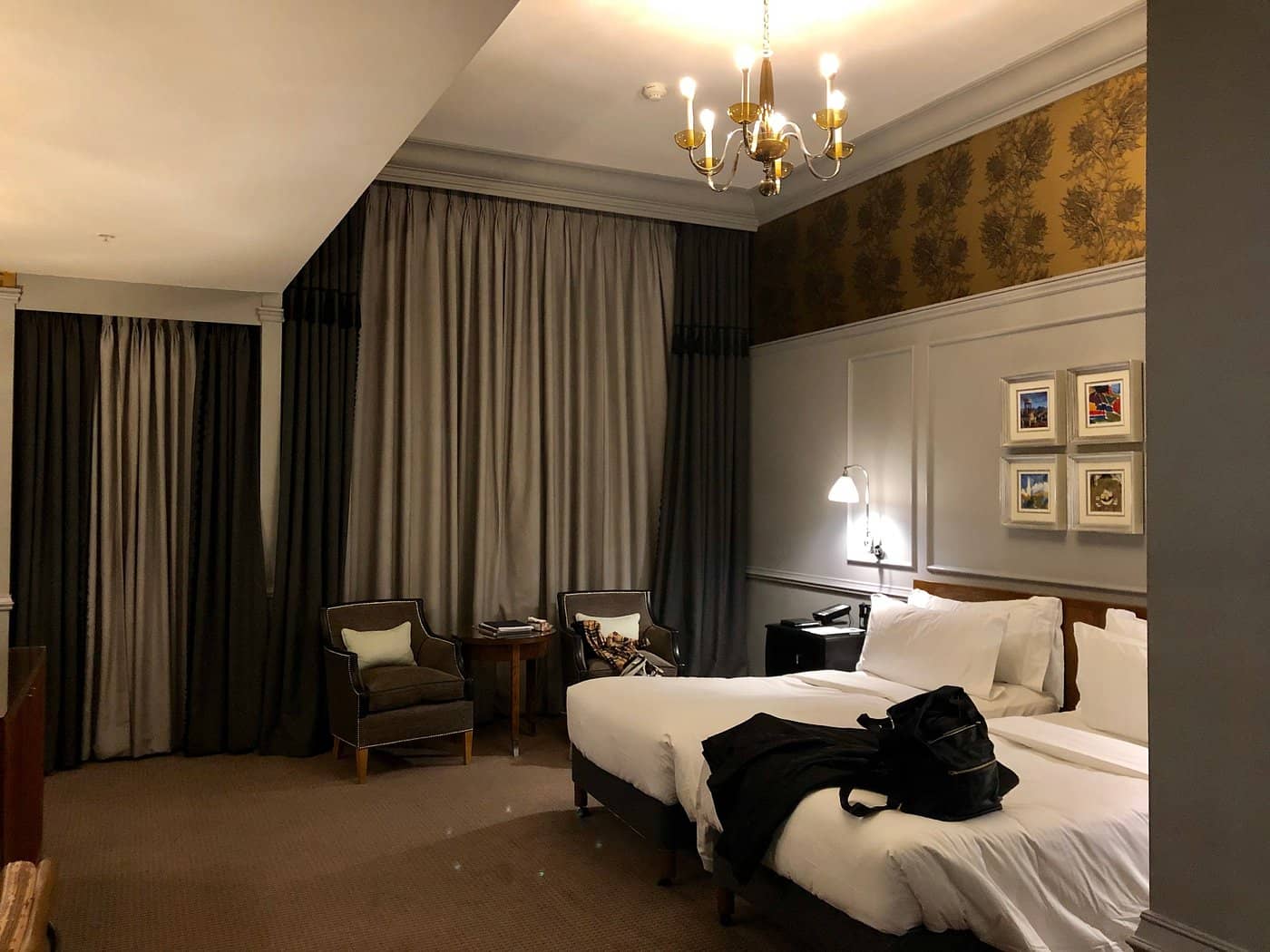 A luxurious room at The Caledonian Edinburgh Curio Collection by Hilton featuring a large comfortable bed with soft lighting classic-style chairs and elegant drapes creating a warm and inviting ambiance