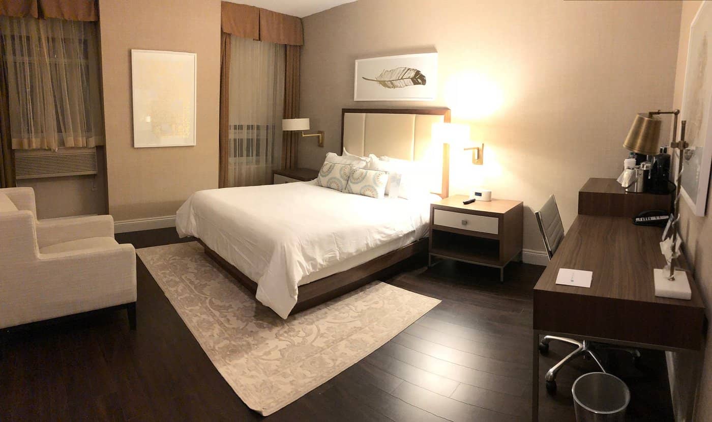 A spacious elegant room at The Lord Nelson Hotel  Suites featuring a comfortable king-size bed soft beige decor wooden flooring a work desk and modern lighting fixtures