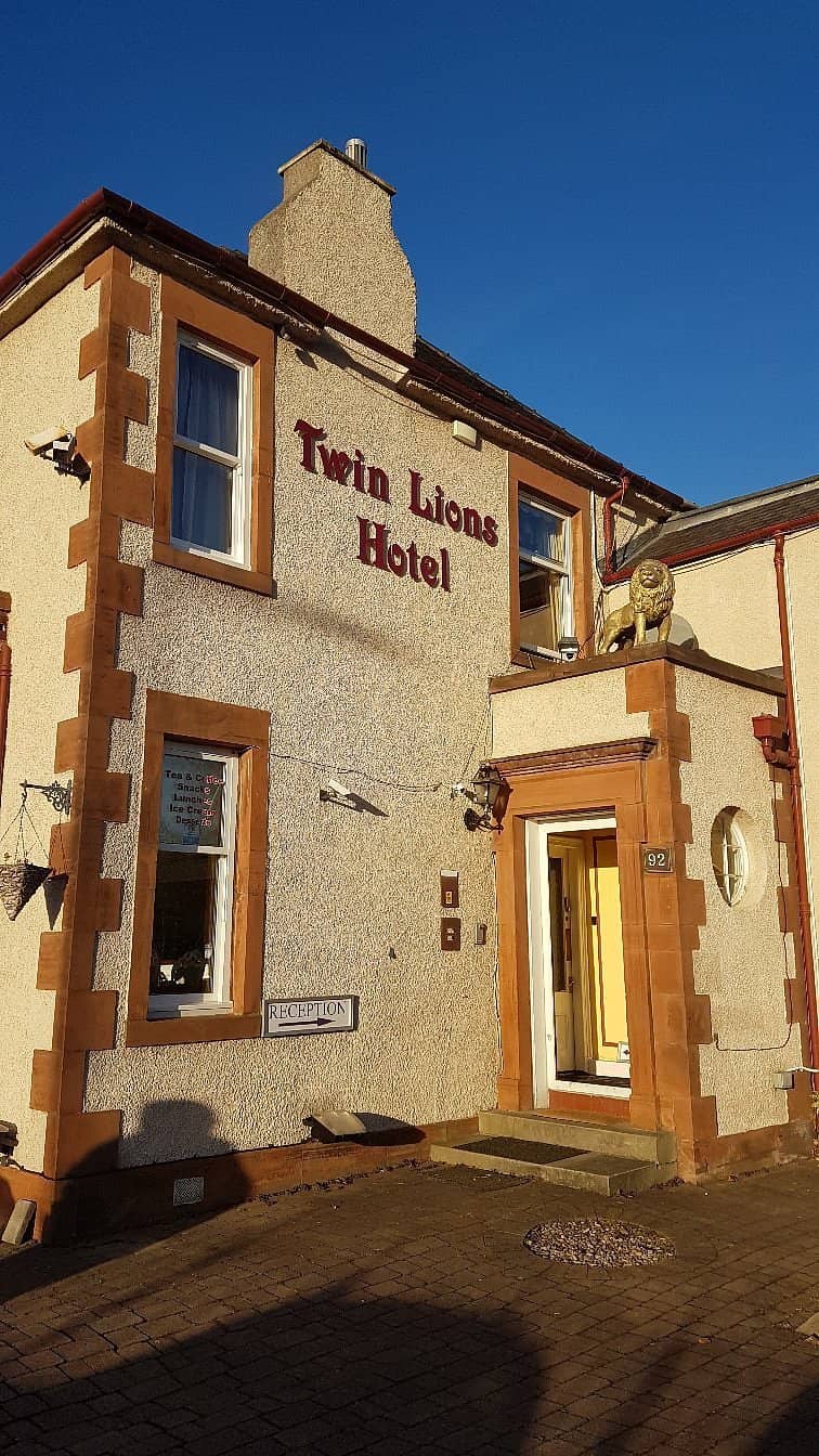 Exterior of Twin Lions Hotel in Edinburgh featuring a traditional building with cream-colored walls red accents and a statue of a lion above the entrance offering cozy accommodations for guests