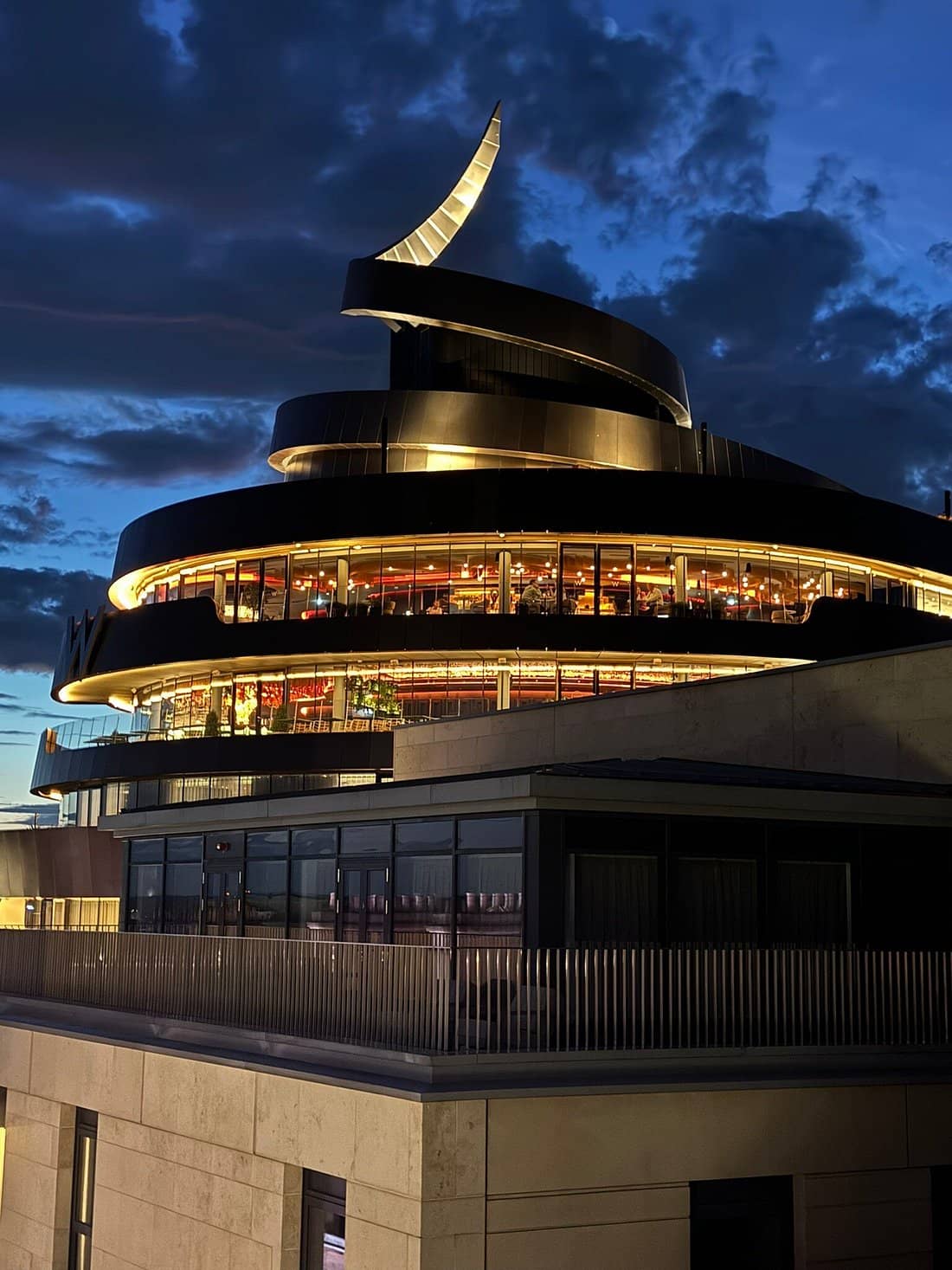 Night view of W Edinburgh showcasing its striking modern architecture with a spiral design and illuminated glass windows creating a vibrant and luxurious ambiance in the city