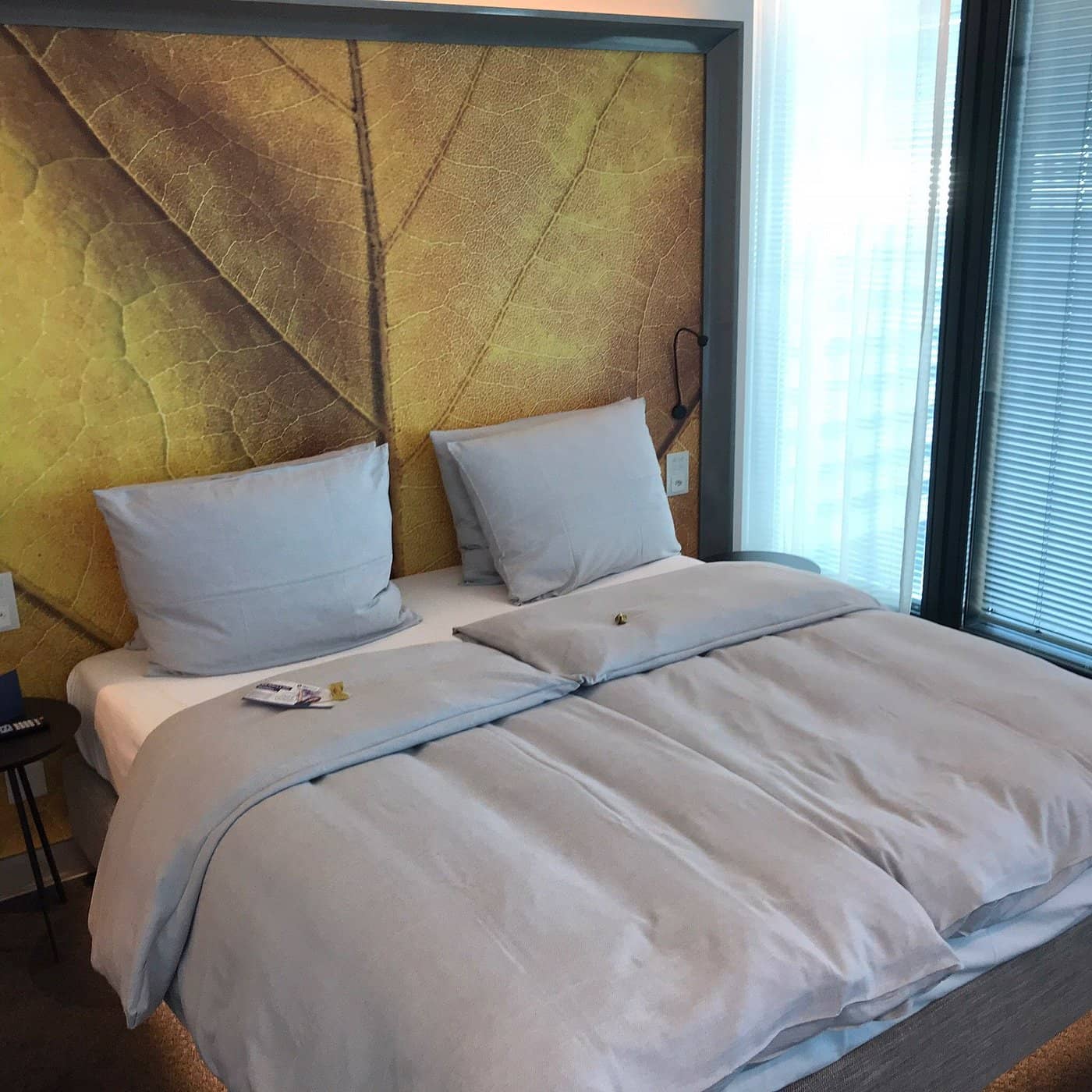 Modern room at HYPERION Basel with a cozy bed soft gray bedding and a large leaf-patterned accent wall