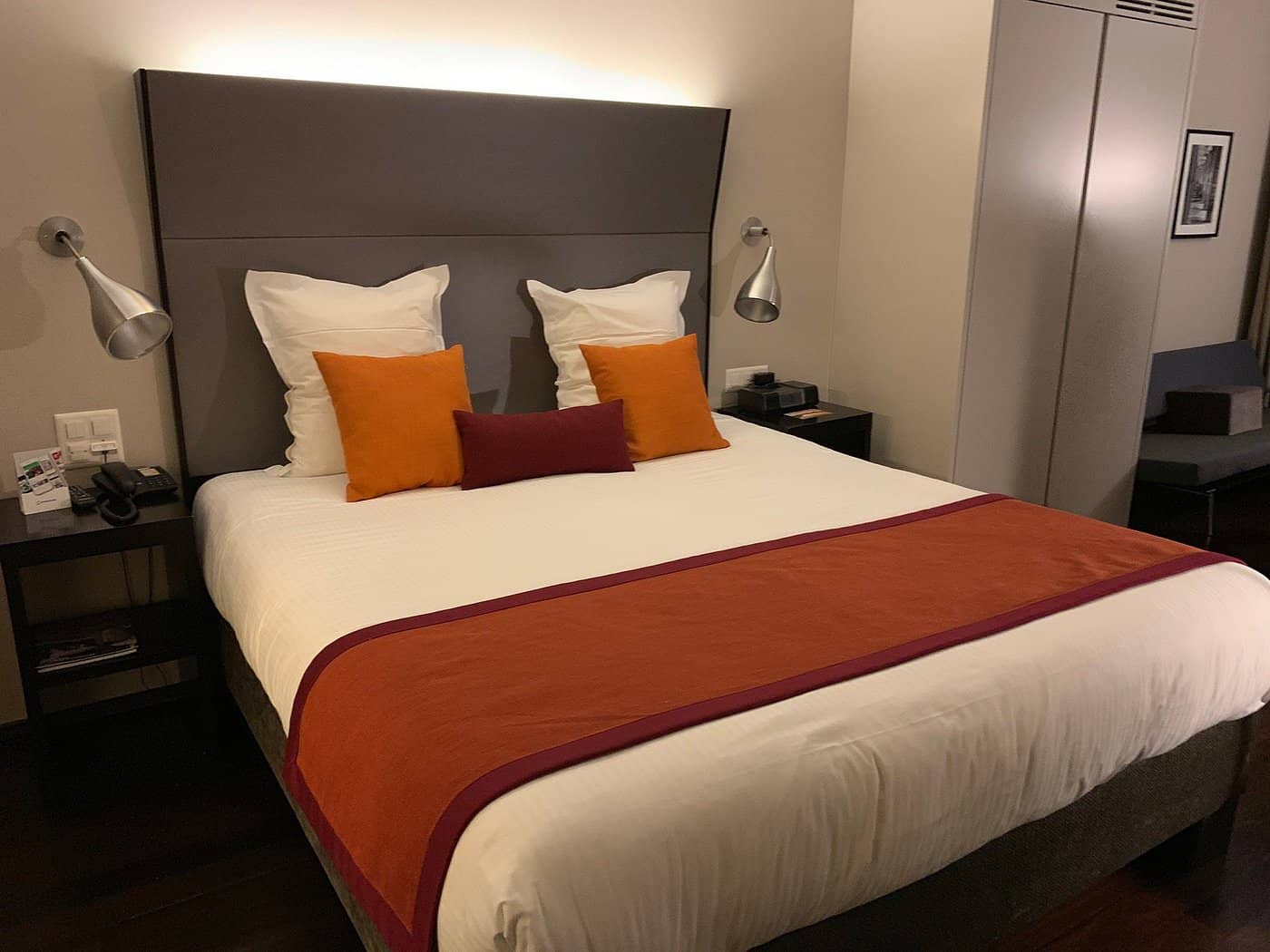 Elegant room at Hotel D Basel featuring a stylish bed with orange and red accent pillows modern bedside lighting and a cozy atmosphere