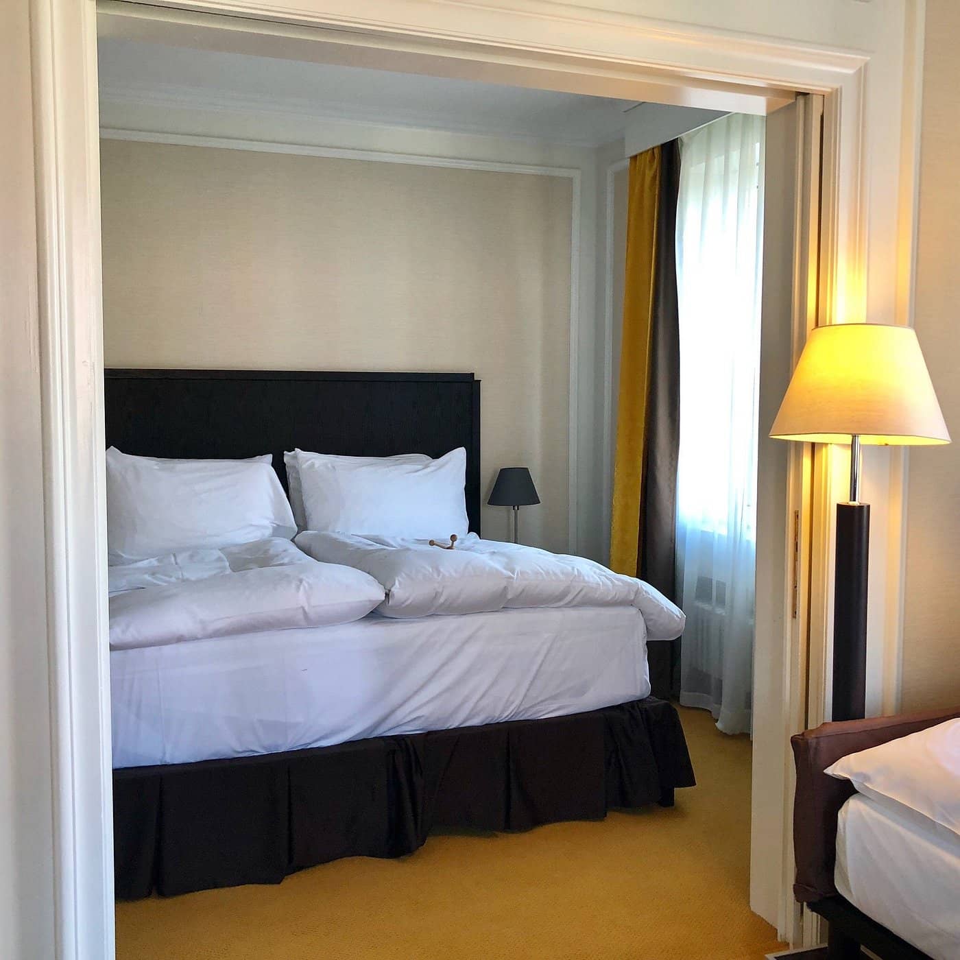 Spacious room at Hotel Euler Basel with a luxurious bed adorned with white linens cozy lighting and warm yellow and gray curtains creating a welcoming ambiance