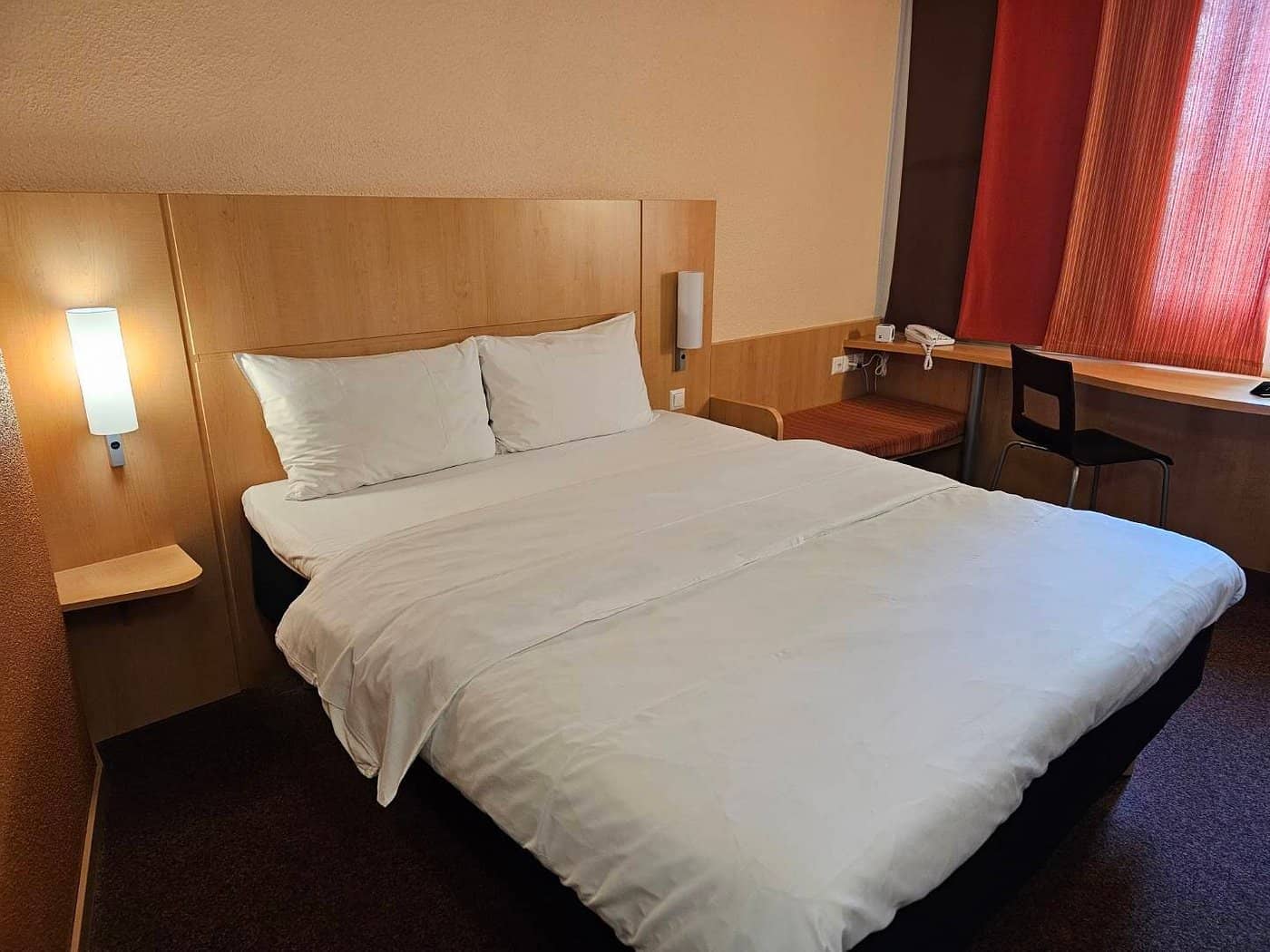 Simple cozy room at Ibis Basel Bahnhof with a comfortable bed wooden accents bedside lighting and a work desk