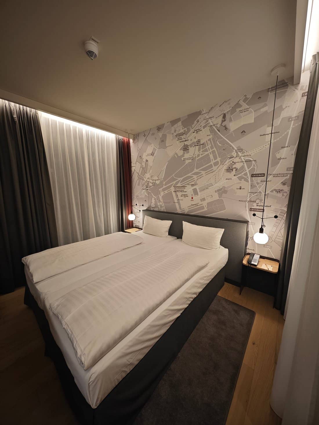The IntercityHotel Berlin Airport BER Terminal 12 room features modern design with cozy bedding and a unique city map wall art