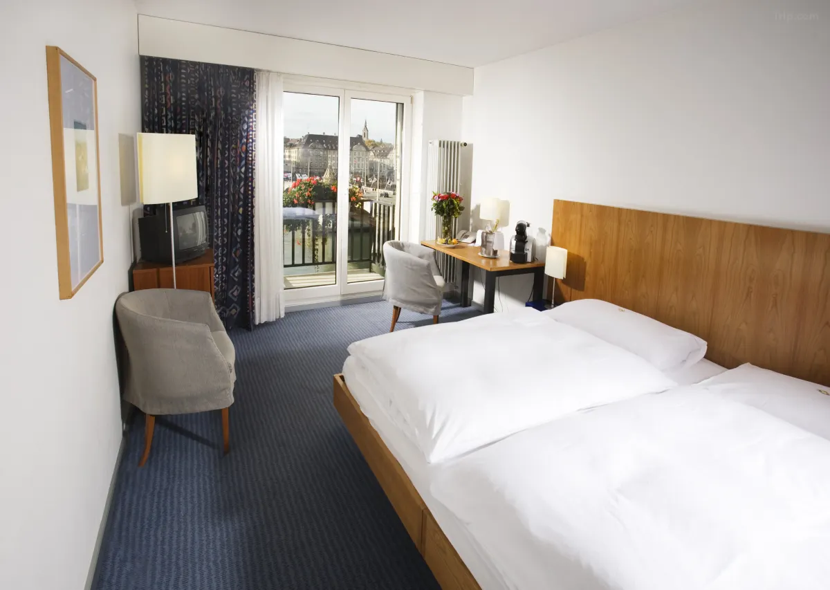 Bright hotel room at Merian Basel - Self Check-In with a cozy bed seating area desk and balcony overlooking the city