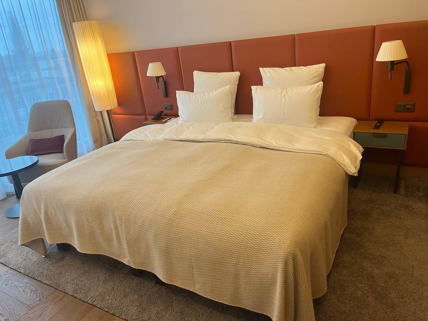 Cozy hotel room at Movenpick Hotel Basel with a large bed warm lighting and modern furnishings including an accent chair and bedside lamps