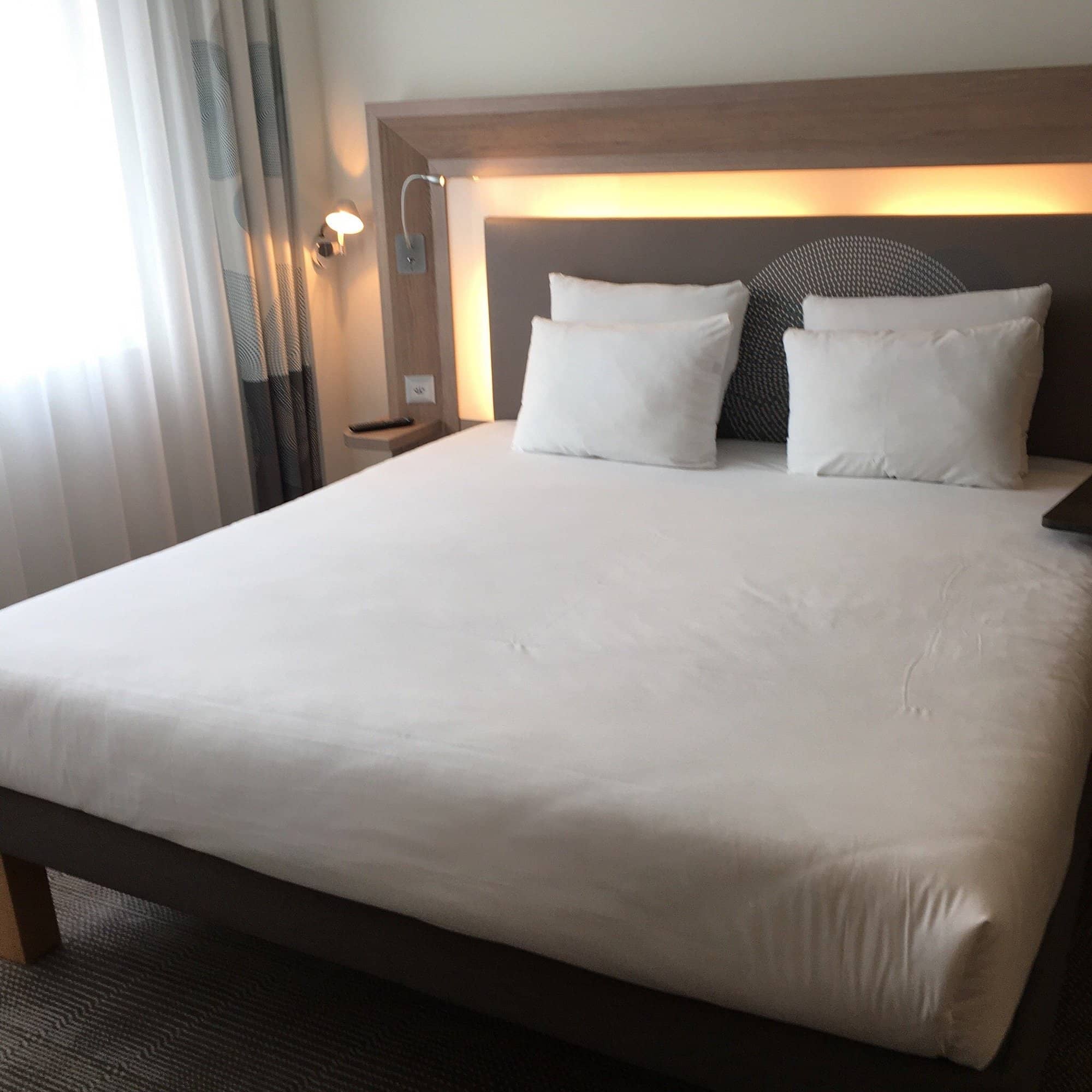 Modern double bed with a light wooden headboard and soft lighting in a comfortable room at Novotel Basel City