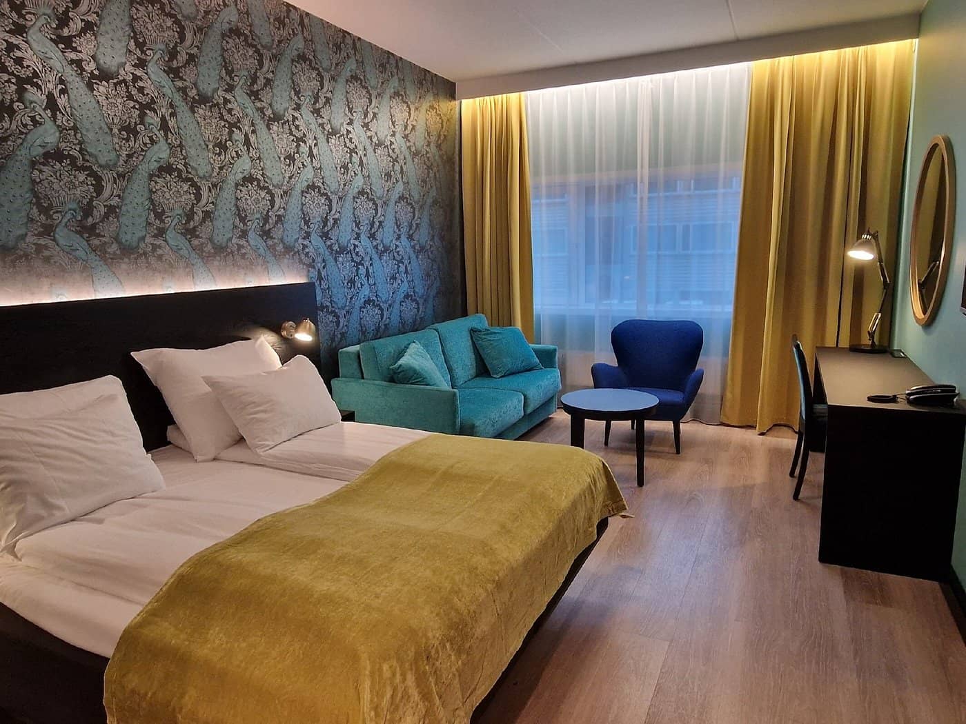 A stylish and vibrant room at Thon Hotel Oslo Airport featuring modern decor with peacock-themed wallpaper a cozy seating area and all amenities needed for a comfortable stay near Oslo Airport